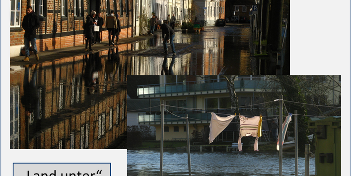 Wasser überflutet die Straße in der historischen Altstadt. Am linken Bildrand bewegen sich Menschen auf dem verbliebenen schmalen Bürgersteig vor den Altstadtfassaden. Auf der rechten Seite säumen Bäume und Laternen die Straße. Im Vordergrund rechts sieht man zum Trocknen aufgehängte Wäsche auf einem Wäscheständer tief im Wasser stehend, im Hintergrund befindet sich ein modernes Wohnhaus.