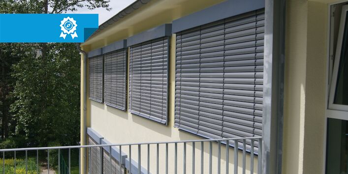 Die Fassade einer Kita wurde fotografiert. Die vier Fenster haben geschlossene Außenjalousien.