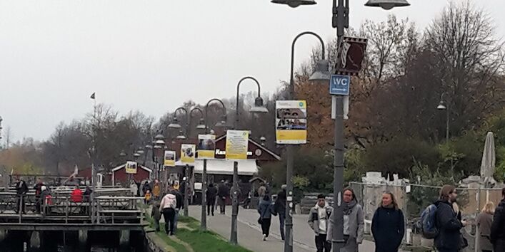 Plakate der Open-Air-Ausstellung ÜberFlut hängen barrierefrei an Laternenpfählen entlang der Hafenspitze in Flensburg.