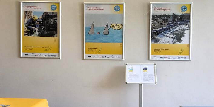 Plakate der Ausstellung ÜberFlut hängen an einer Wand im Geographischen Institut der Uni Kiel. Infoständer mit Begleittexten.