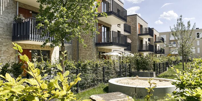 Der Blick geht auf die Außenanlagen und Gärten des Eigentumsbereichs. Die Wohngebäude haben Balkone, helle Klinkerfassaden.