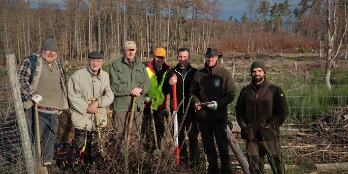 Es stehen sieben Personen in einer Waldfläche. Vier personen halten einen Spaten.