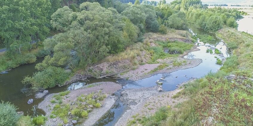 Aerial view of the Fulda and a branch with low water flow. Grasses, shrubs and trees grow on the banks with diverse hydromorphological structures.