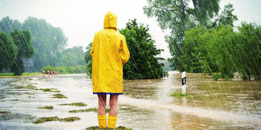 Frau steht mit Regenjacke und Gummistiefeln in einem überschwemmten Gebiet