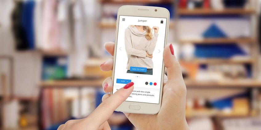 eine Frau bestellt vor ihrem Kleiderschrank mit ihrem Smartphone Kleidung