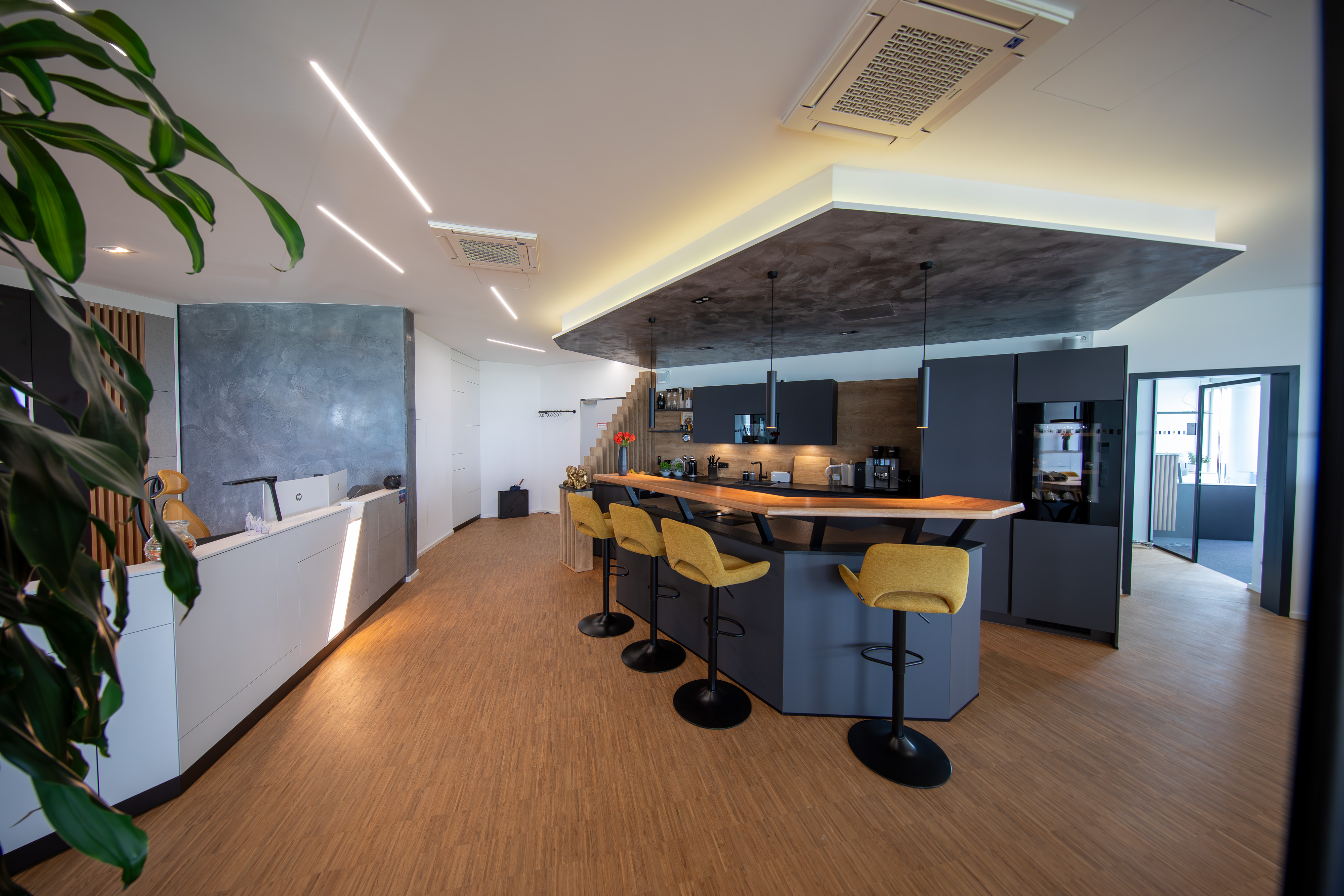 Der Empfangsbereich des Bürogebäudes mit einem Tresen und Barhockern sowie den Klimageräten an der Decke.