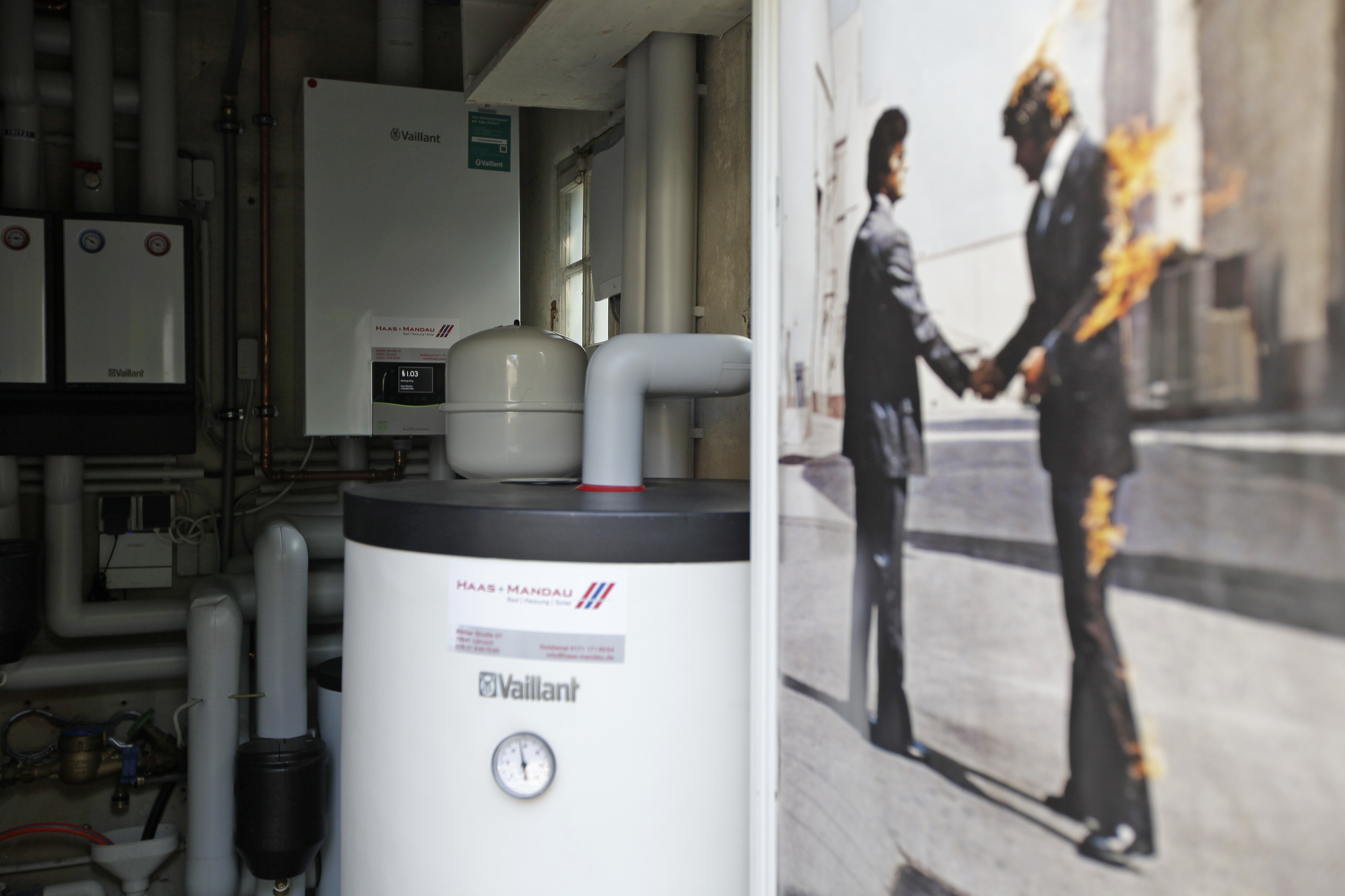 Blick in den Technikraum mit der wandhängenden Gas-Brennwertanlage im Hintergrund, davor der Pufferspeicher und ein Filmplakat