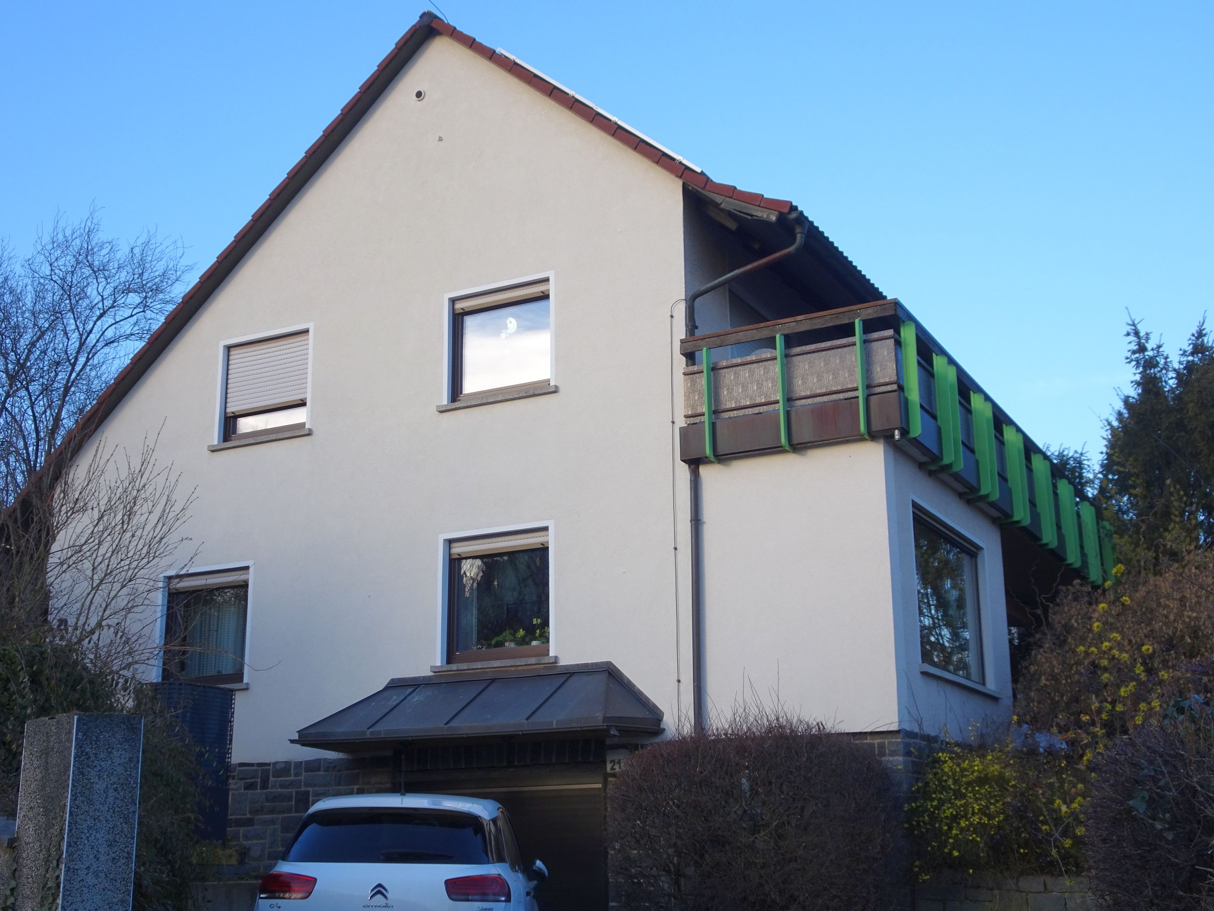 Das Gebäude von Südost mit dem Balkon über die gesamte Gebäudelänge, die Effizienz-Wärmepumpe steht unterhalb der linken Fenster