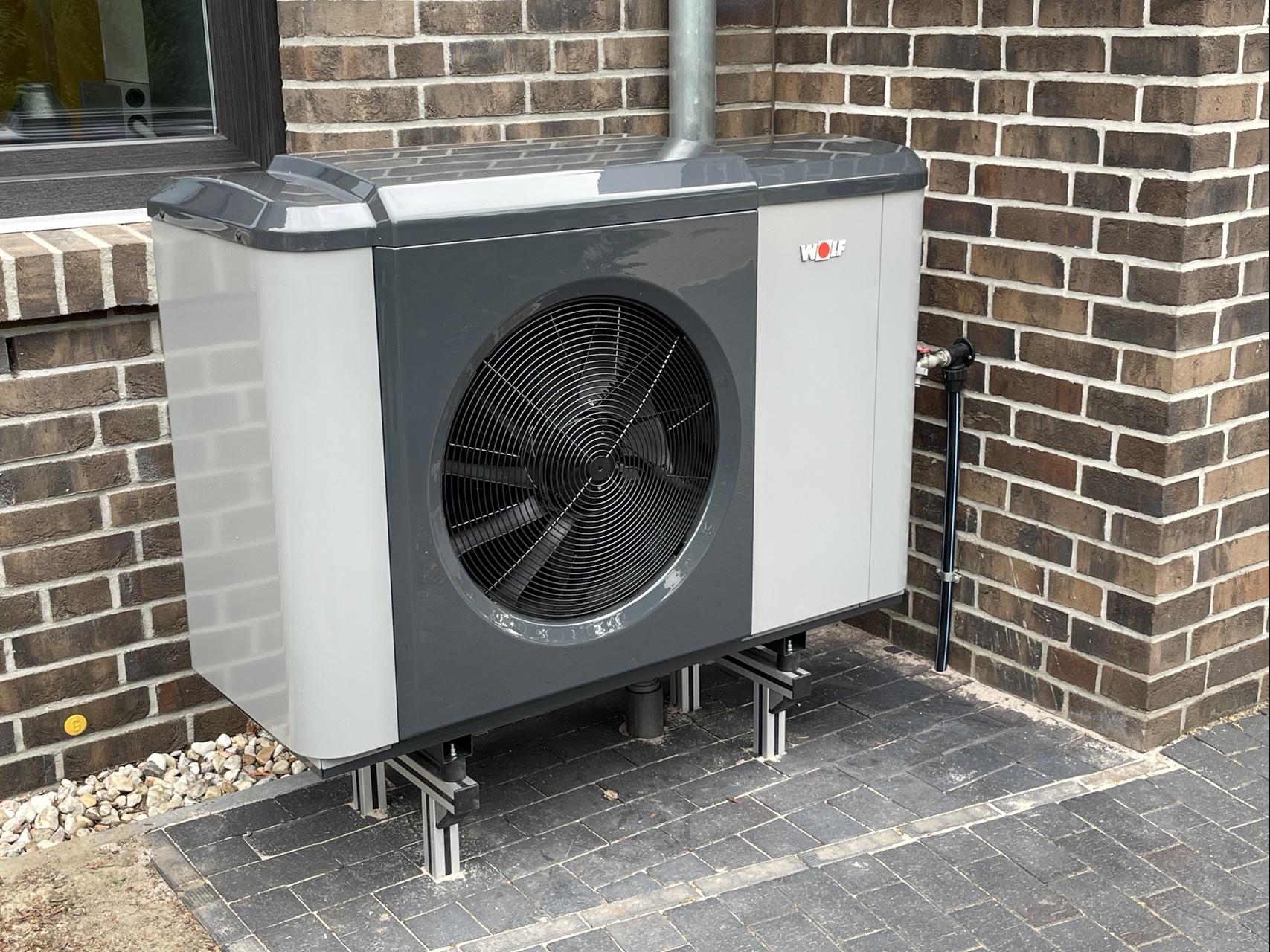 Die Außeneinheit der Wärmepumpe in einer Nische vor Klinker-Mauerwerk.