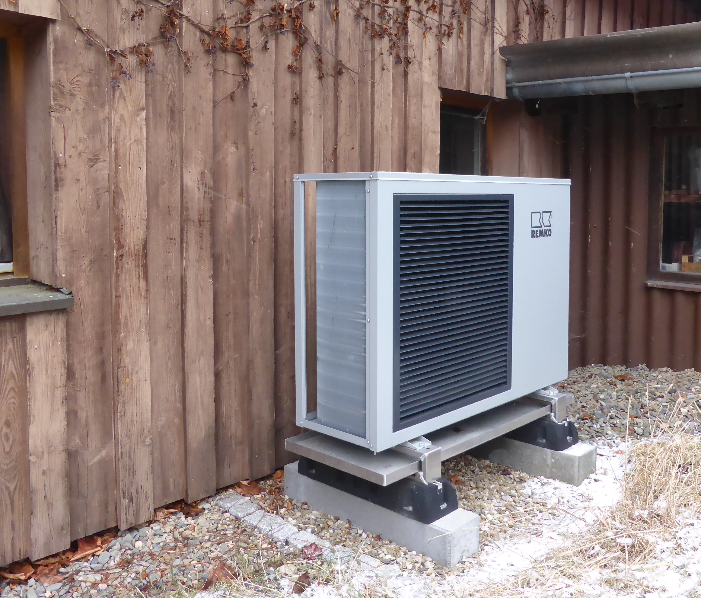 Die Außeneinheit einer Wärmepumpe an einer Holzfassade.